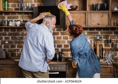 Back view of mature couple having fun while cleaning kitchen appliances - Powered by Shutterstock