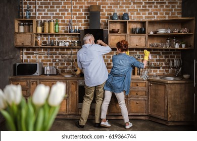 Back View Of Mature Couple Having Fun While Washing Dishes In Kitchen 