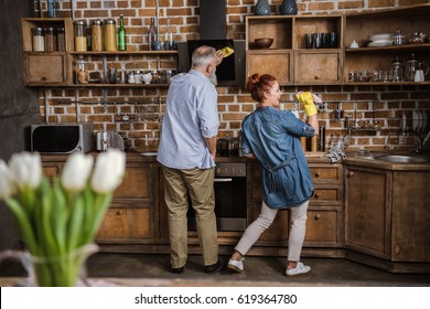 Back View Of Mature Couple Having Fun While Washing Dishes In Kitchen 