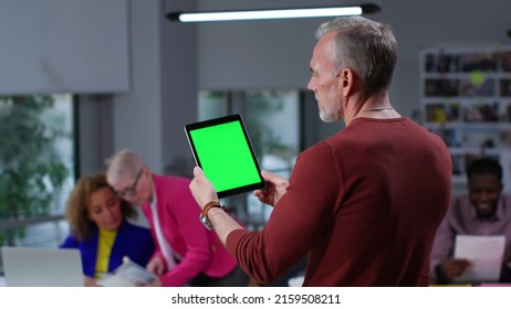 Back view of mature man holding digital tablet with green screen standing in modern office. Entrepreneur work on tablet computer