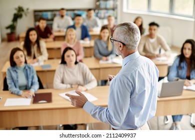 Back view of mature professor giving lecture to large group of college students in the classroom. - Shutterstock ID 2112409937