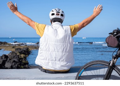 Back view of mature senior man with outstretched arms sitting in front to the sea. Elderly man wearing helmet close to his bike - Powered by Shutterstock