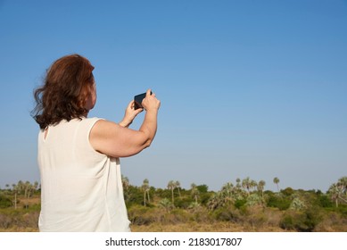 Back View Of A Mature Woman Taking Photos With Her Phone In El Palmar National Park, Entre Rios, Argentina. Concepts: Nature Travel, Vacation Pictures, Enjoying The Outdoors, Active Life.