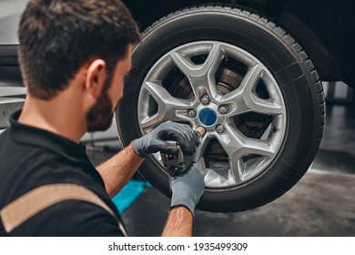 Back View Of Mechanic Is Repairing Car At Service Station. Close Up View Of Repairman Is Removing Wheel By Electric Wrench, Tyre Mounting Equipment At Workshop Auto Repair Shop. Tire Fitting Concept.