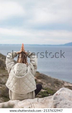 Back view of meditate young girl  at mountain cliff. Peace, meditation and mindfulness. Vertical photo.