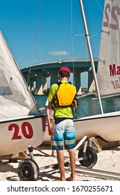 Back view, medium distance  of a young male, with safety vest, preparing a trailered sailing boat, on a tropical shoreline