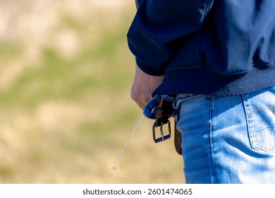 Back view of a men standing on the sidewalk and peeing in the forest against the tree trunk, Selective focus of low angle of a man in blue jean is urinating outdoor along gravel walkway in countryside