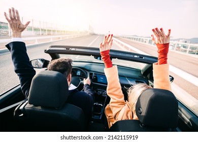 Back view of middle age couple raising their hands up while driving a car on road trip. Happy 40s man and woman - Powered by Shutterstock