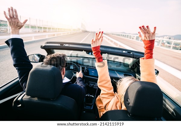 Back view of\
middle age couple raising their hands up while driving a car on\
road trip. Happy 40s man and\
woman