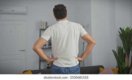 Back view of a middle-aged man with hands on hips standing in a modern living room, contemplating. - Powered by Shutterstock