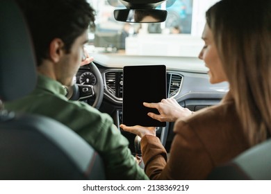 Back View Of Millennial Couple Using Digital Tablet With Empty Screen, Sitting In Their New Car At Dealership, Mockup For Navigation App Design. Touch Pad Website Template