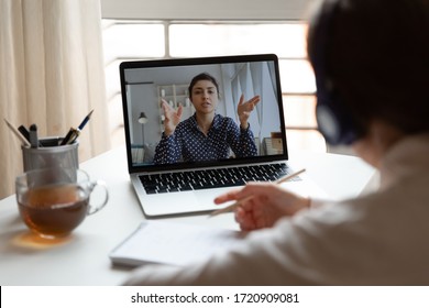 Back View Of Millennial Girl In Headphones Listen Watch Online Training Or Course On Laptop, Female Employee Make Notes Engaged In Webcam Conference Or Briefing With Colleague, Have Web Meeting At