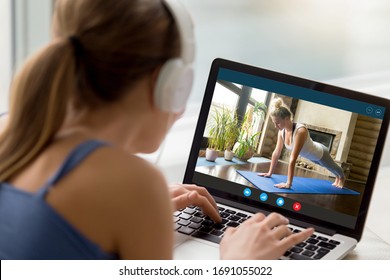 Back view of millennial girl relax at home enjoy yoga online training practice course on laptop, young woman watch fitness sports workout video using modern internet application on computer