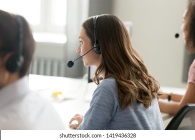 Back view of millennial woman employee wearing headset with microphone busy working in shared office, smiling female worker or call center agent consulting clients over internet giving help