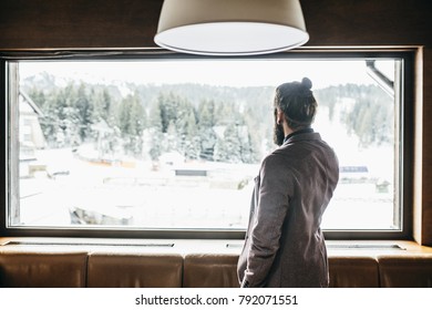 Back View Of Modern Businessman Standing At Log Cabin And Looking Through Window.