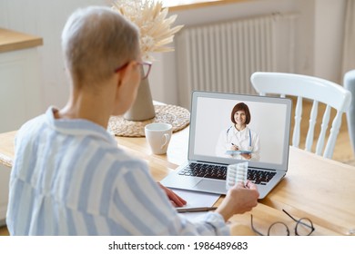 Back View Of Modern Focused Middle Aged Woman Having Online Call With Doctor On Laptop During Covid 19 Outbreak, Showing Pills Sitting In Kitchen At Home. Healthcare And Medicine Concept