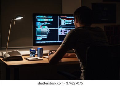 Back view of modern programmer sitting and writing code in dark room