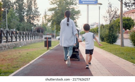 Back View Of Mom Pushing Stroller And Holding Preschooler's Hand