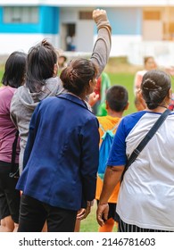 Back View Of Moms Watch And Cheering Their Sons Playing Football In School Tournament On Sideline. Sport, Outdoor Active,  Spectator Watching Soccer Game. Parents Care And Encourage Their Children.