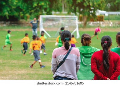 Back View Of Moms Watch And Cheering Their Sons Playing Football In School Tournament On Sideline. Sport, Outdoor Active,  Spectator Watching Soccer Game. Parents Care And Encourage Their Children.