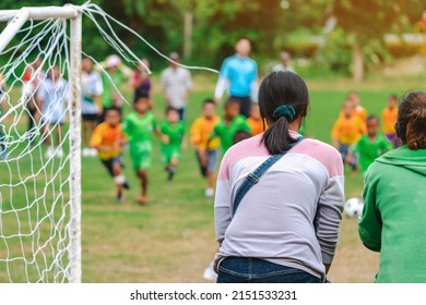 Back view of Moms watch and cheering their sons playing football in school tournament on sideline. Sport, outdoor active,  Spectator watching soccer game. Parents care and encourage their children.