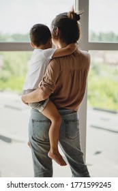 Back View Of Mother Holding Child In Her Arms.