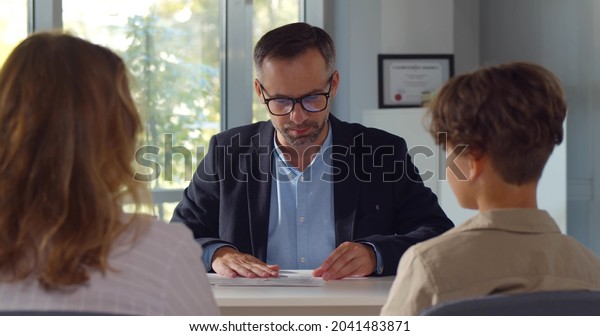 Back view of mother and son having interview with\
school headmaster. Mature male principal have meeting with\
schoolboy and parent in\
office