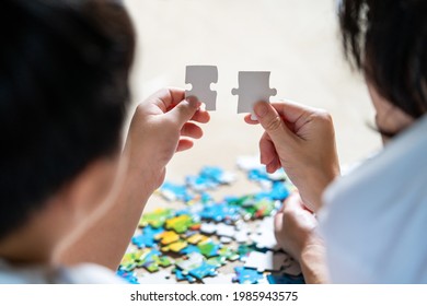 Back view of mother and son lying on the floor holding puzzle pieces and putting them together. Happy family during work at home. Woman teaches child to solve puzzles. Parent and cheerful concept	