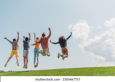 Back View Of Multicultural Kids Jumping And Gesturing Against Blue Sky 