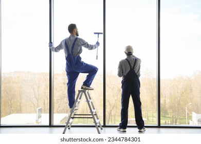 back view of multicultural professional workers washing large panoramic windows in office.