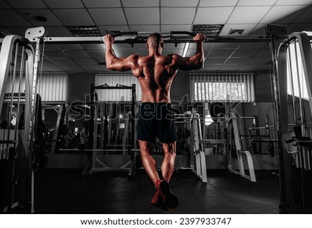 Back view of Muscular man doing pull up on horizontal bar in gym, working out. Strong fitness male pulling up, showing back