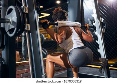 Back View Of A Muscular Young Curly-haired Woman Doing The Barbell Back Squat In The Power Rack