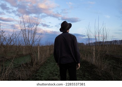 Back view of a mysterious man in a hat walks in a field of dry grass. Dark sky with clouds. - Powered by Shutterstock