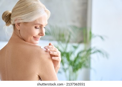 Back view of naked gorgeous middle aged 50s woman applying moisturizing body lotion after shower. Advertising of bodycare spa procedures, antiage sun protection treatment products concept.