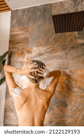 Back View Of Naked Young Woman Washing Her Hair Using Organic Natural Shampoo While Taking Shower In Marble Bathroom. Spa, Beauty And Body Care Concept. Mature Content