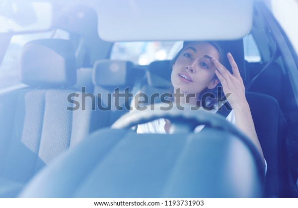 back view of nice stylish woman driver looking at a\
rear view mirror and correcting the hairstyle and makeup while\
driving the car