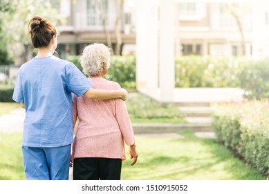 Back View Of Nurse Caregiver Support Walking With Elderly Woman Outdoor