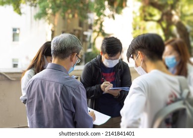 Back View Of Old Professor With Grey Hair And Glasses Teaches Discuss Small Group University Students Of Boy And Girl With Face Mask About Field Tests In Urban Environment. All Taking Notes