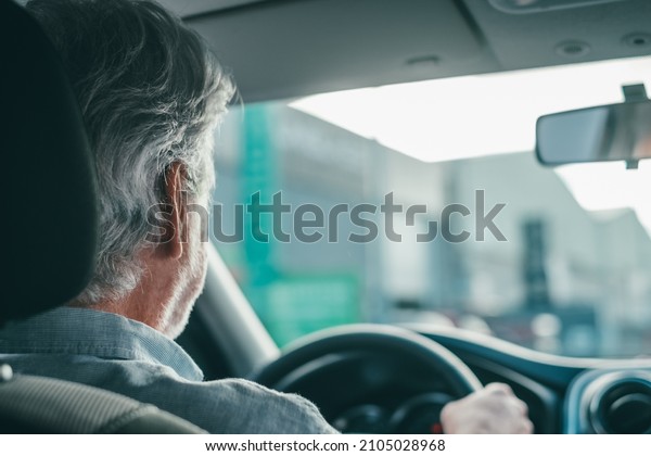 Back view of old retired man driving in the street\
with his car.