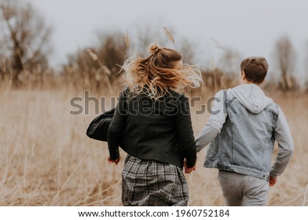 Back view on couple two people friend running run away in dry grass meadow field in spring sepia beige colors blurred in background blond hair waving in wind freedom concept symbol