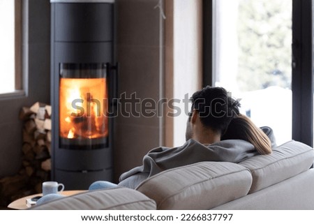 Back view on cute lovers sitting on the couch close to fireplace. Young couple spending time together in the cozy home