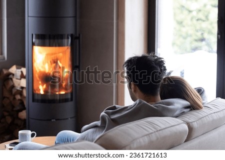 Back view on cute lovers sitting on the couch close to fireplace. Young couple spending time together in the cozy home