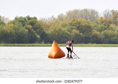 Back View On Teenager Boy Rowing On SUP (stand Up Paddle Board) In Danube River Near Buoy. Racing Competitions On SUP