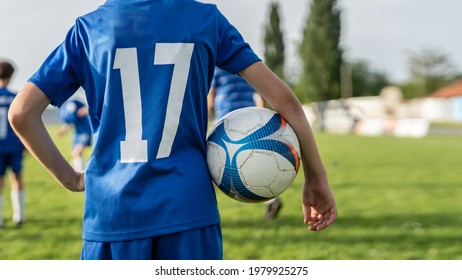 Back View On Unknown Boy Standing With Ball On The Soccer Football Field In Sunny Day During Training Or Game Wearing Blue Uniform And Number 17 With Copy Space