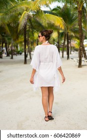 Back View On Woman On Tropical Vacation At Caribbean Resort Beach. Brunette Model Wearing Summer Fashion Sunglasses And White Kaftan. Riviera Maya, Mexico.