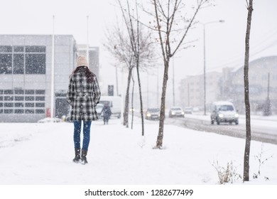 Back View On Women Walking In The City On Blizzard. Woman Walks Through Snow On Sidewalk