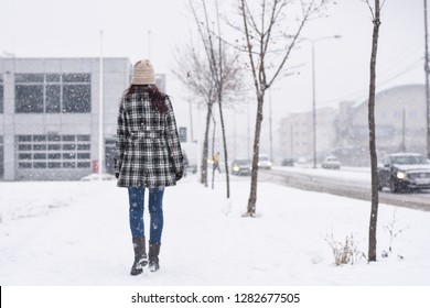 Back View On Women Walking In The City On Blizzard. Woman Walks Through Snow On Sidewalk