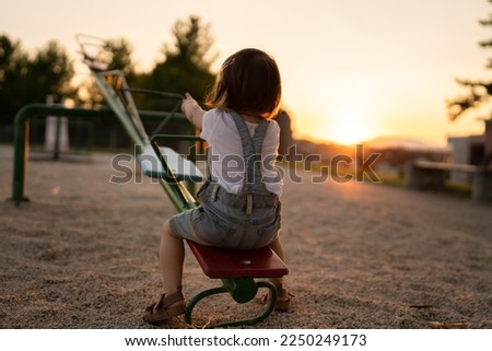 back view of one small caucasian toddler child sitting alone on the seesaw in park in sunset lonely with no friends copy space childhood growing up concept social issues rejected