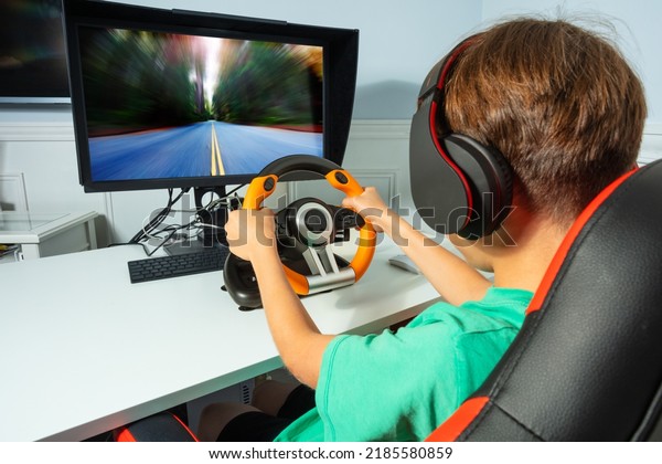 Back view over the shoulder of a\
gamer boy, hands on steering wheel play race game on\
computer