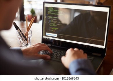 Back view over the shoulder shot of developer programmer with laptop. Program code and script data on the screen. Young freelancer in glasses working on project in cafe.